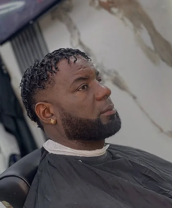 Cliente de perfil con twists arriba, laterales degradados y barba completa perfilada