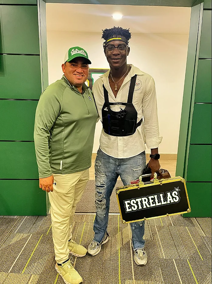 Yeron con chaleco portaherramientas de barbero y un maletín de Estrellas, junto a una persona con gorra de Estrellas